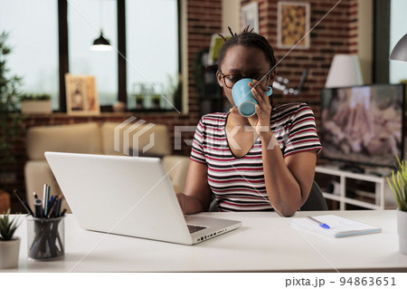 Remote student watching educational tutorial on laptop at home, drinking coffee. Woman attending online courses class, young freelancer working on internet, holding tea mug Remote student watching educational tutorial on laptop at home, drinking coffee. Woman attending online courses class, young freelancer working on internet, holding tea mug 94863651