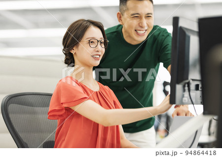 オフィスで先輩に仕事を教えてもらう女性 94864418