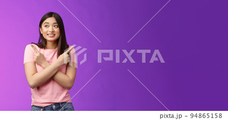 Cheerful timid cute asian girl, look tender, smiling gazing aside cross hands chest, pointing sideways, show left right, making decision, gathering confidence choose, purple background 94865158