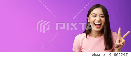 Headshot sincere carefree laughing asian girl having fun, show peace victory sign, joyfully look camera, express enthusiasm and happiness, enjoy funny friendly company, stand purple background 94865247