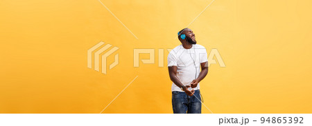 Full length portrait of a cherry young african american man listening to music with headphones and dancing isolated over yellow background 94865392