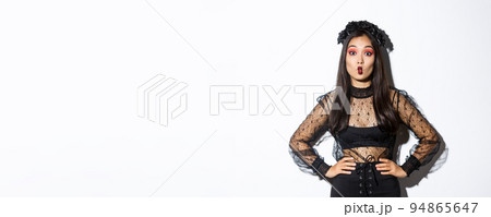 Portrait of silly attractive asian woman fooling around, showing funny faces at camera while wearing halloween costume, standing over white background 94865647