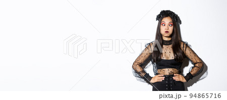 Portrait of funny and carefree asian girl having fun on halloween, making faces and holding breath, standing in gothic witch costume over white background 94865716