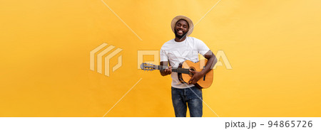 Full-length photo of excited artistic man playing his guitar. Isolated on yellow background. 94865726