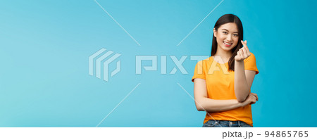 Cheerful cute asian woman dark short haircut, show korean heart sign with fingers, smiling joyfully, express sympathy and caring feelings, confess love stand blue background, grinning upbeat 94865765
