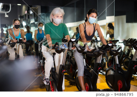 Young and mature female in masks warming up on bikes Young and mature female in masks warming up on bikes 94866795