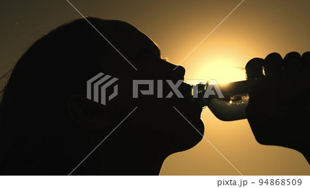 silhouette girl drinking water from bottle glare sun. man quenches thirst sunset. wants drink energy drink dawn. sport drinking water. man outdoors drinks water. healthy lifestyle drinking regime 94868509