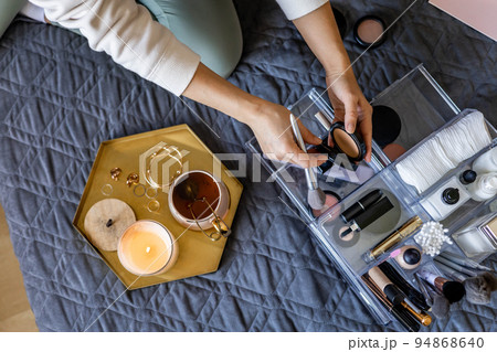 Woman hands tidying up putting powder container into acrylic storage box makeup products placement 94868640