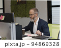 A European adult man with a beard works at a computer in the office of company 94869328