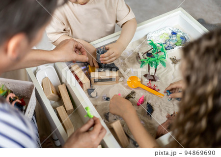 Closeup woman parent and children hands playing early development sensory sand box with dinosaurs 94869690