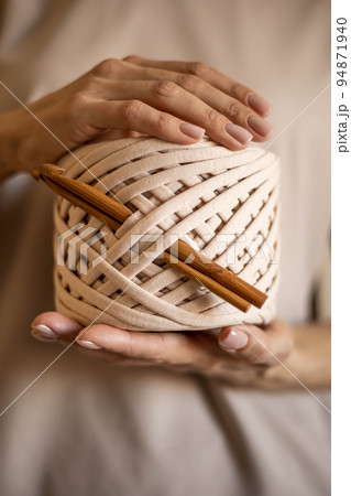 Closeup beautiful female hands hold hank reel of beige ribbon yarn and wooden crochet needles 94871940