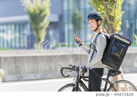 スマホを手に持ってロードバイクを引いているフードデリバリー 女性配達員 スマホを手に持ってロードバイクを引いているフードデリバリー 女性配達員 94872826