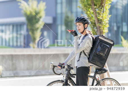 ロードバイクを引いてスマホに話しかけているフードデリバリー　女性配達員 94872939
