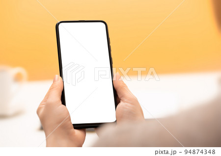 Mockup mobile cell phone. hands of woman with cell phone against background of yellow wall and cup of coffee. female hand holding using mobile on desk at cafe 94874348