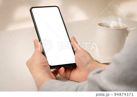 Mockup phone. Close up hand holding cellphone smartphone with blank screen in coffee shop. Woman hand using mock up smart phone at coffee shop 94874371