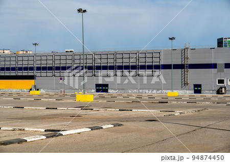 large industrial warehouse. parking large warehouse. Exterior view of large warehouse. empty parking lot in front of large gray industrial building large industrial warehouse. parking large warehouse. Exterior view of large warehouse. empty parking lot in front of large gray industrial building 94874450