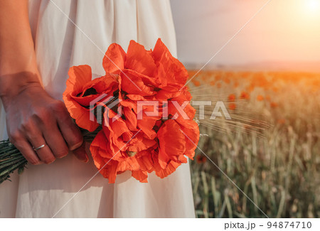 Bride in a white dress holding a bouquet of poppy flowers, warm sunset time on the background of the red poppy field. Copy space. The concept of calmness, silence and unity with nature. 94874710