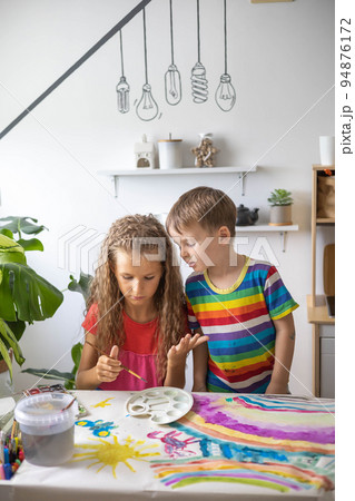 Confident cute boy and girl art drawing multicolored rainbow arch use paints and brush on table Confident cute boy and girl art drawing multicolored rainbow arch use paints and brush on table 94876172
