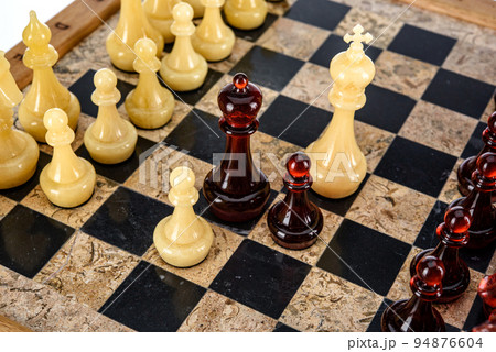 Natural amber different chess pieces figures standing on brown stone board. Close up game concept competition, Classic Gambit Tournament of confrontation. Natural amber different chess pieces figures standing on brown stone board. Close up game concept competition, Classic Gambit Tournament of confrontation. 94876604