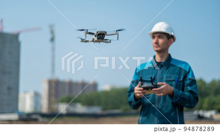 A man in a helmet and overalls controls a drone at a construction site. The builder carries out technical oversight. 94878289