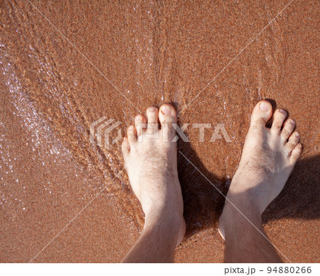 Top view of men's legs in the sea. A man is standing on the sand. Top view of men's legs in the sea. A man is standing on the sand. 94880266