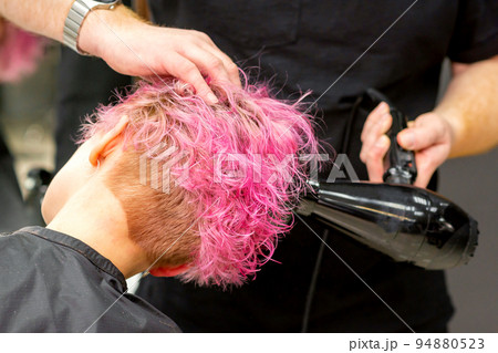 Drying short pink bob hairstyle of a young caucasian woman with a black hair dryer with the brush by hands of a male hairdresser in a hair salon, close up Drying short pink bob hairstyle of a young caucasian woman with a black hair dryer with the brush by hands of a male hairdresser in a hair salon, close up 94880523