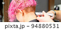 Male hairdresser shaves neck of a young caucasian woman with a short pink hairstyle by electric shaver in a hairdresser salon, close up 94880531