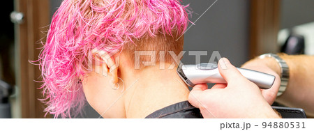 Male hairdresser shaves neck of a young caucasian woman with a short pink hairstyle by electric shaver in a hairdresser salon, close up Male hairdresser shaves neck of a young caucasian woman with a short pink hairstyle by electric shaver in a hairdresser salon, close up 94880531