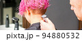 Male hairdresser shaves neck of a young caucasian woman with a short pink hairstyle by electric shaver in a hairdresser salon, close up 94880532