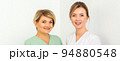 Close-up portrait of two young smiling female caucasian healthcare workers standing staring at the camera on white background 94880548