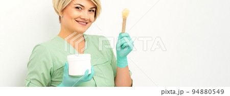 The master of sugar hair removal holds liquid yellow sugar paste, wax for depilation with the jar on a wooden stick on a white background The master of sugar hair removal holds liquid yellow sugar paste, wax for depilation with the jar on a wooden stick on a white background 94880549