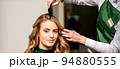 Hairdresser combing long hair of young caucasian woman looking at the camera and smiling in beauty salon 94880555