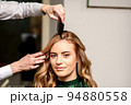 Hairdresser combing long hair of young caucasian woman looking at the camera and smiling in beauty salon 94880558
