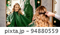 Hairdresser combing long hair of young caucasian woman looking and smiling in the mirror in beauty salon 94880559