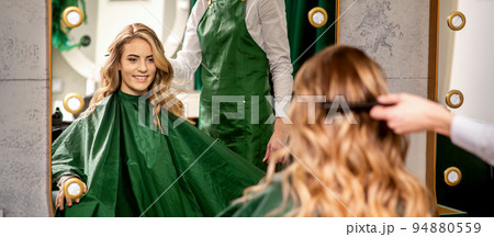 Hairdresser combing long hair of young caucasian woman looking and smiling in the mirror in beauty salon 94880559