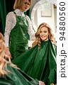 Hairdresser combing long hair of young caucasian woman looking and smiling in the mirror in beauty salon 94880560