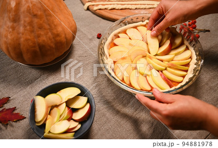 Close-up of the hands of a housewife, spreading apple slices in a circle on top of pumpkin puree in rolled out dough in the baking dish, while preparing a tasty pumpkin pie for Thanksgiving Day 94881978