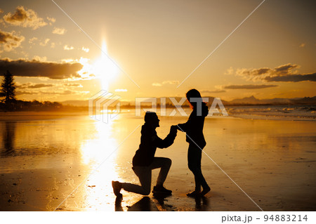 夕日の海辺でプロポーズする男性と受ける女性のシルエット 94883214