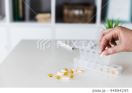 Closeup of female elderly hands sorting, organizing pills. Medical pill box with doses of tablets for daily take with white, yellow, beige drugs, capsules. Young woman get her daily vitamins at home 94884285