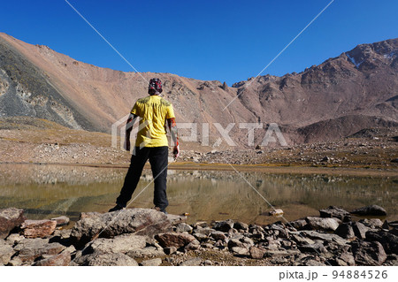 The guy stands epically on shore of mountain lake The guy stands epically on shore of mountain lake 94884526