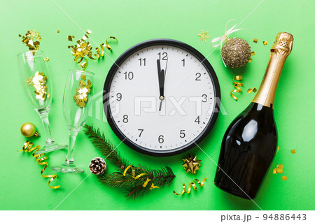 New year celebration concept with a bottle of champagne and two glasses toasting. Christmas gift box, alarm clock and fir tree branch on colored table. Top view Copy space New year celebration concept with a bottle of champagne and two glasses toasting. Christmas gift box, alarm clock and fir tree branch on colored table. Top view Copy space 94886443