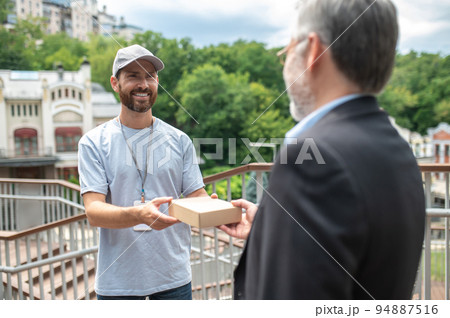 Young male courrier giving the box to the mature businessman Young male courrier giving the box to the mature businessman 94887516