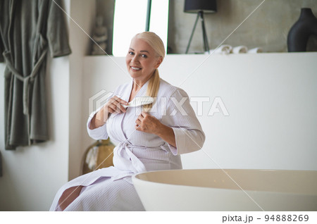 Joyous beautiful lady combing her ponytail with a hairbrush 94888269
