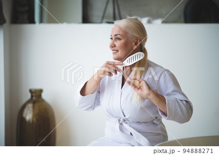 Joyful female brushing her hair seated in the bathroom Joyful female brushing her hair seated in the bathroom 94888271