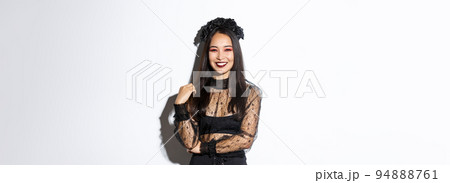 Beautiful young happy woman enjoying halloween party, smiling and looking cheerful while wearing her evil witch costume for trick or treating, standing over white background Beautiful young happy woman enjoying halloween party, smiling and looking cheerful while wearing her evil witch costume for trick or treating, standing over white background 94888761