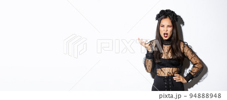 Frustrated and angry young asian woman in witch dress arguing with someone, looking pissed-off and bothered, shaking hand and looking scary at camera, standing over white background Frustrated and angry young asian woman in witch dress arguing with someone, looking pissed-off and bothered, shaking hand and looking scary at camera, standing over white background 94888948