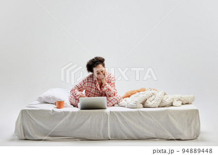 Portrait of young charming girl in home wear sitting on bed at home isolated on gray background. Ideas, inspiration, imagination. Art, beauty, youth 94889448