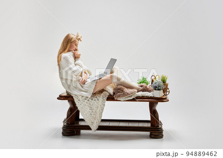 Young beautiful girl sitting at wooden table and using laptop isolated over grey background. Ideas, inspiration, imagination. Retro, vintage style 94889462