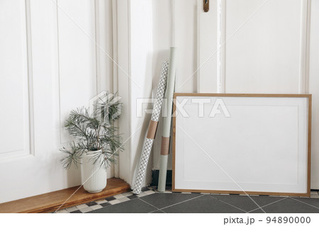 Festive Christmas indoor decor. Blank horizontal wooden picture frame mockup on dark tiled floor. Pine tree branches in vase, gift wrapping papers. White hall background. Empty artistic template. Festive Christmas indoor decor. Blank horizontal wooden picture frame mockup on dark tiled floor. Pine tree branches in vase, gift wrapping papers. White hall background. Empty artistic template. 94890000