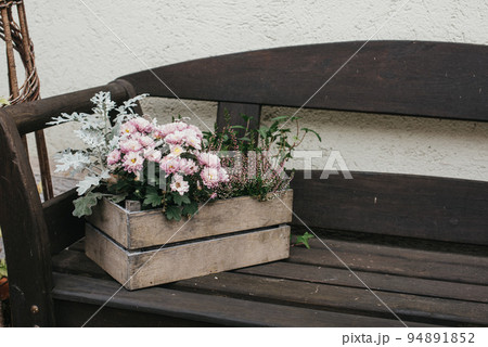 Vintage Outdoor Furniture, Mums And Nik-naks. Wooden Bench In Front Garden With Flower Boxes. Box With Flowers On The Bench. Wooden Bench In Front Garden With Flower Boxes. Box With Flowers On The Vintage Outdoor Furniture, Mums And Nik-naks. Wooden Bench In Front Garden With Flower Boxes. Box With Flowers On The Bench. Wooden Bench In Front Garden With Flower Boxes. Box With Flowers On The 94891852